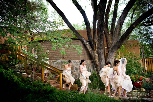 beautiful photo of the bride and bridesmaids standing in a garden area waiting for their cue to enter the ceremony - bride is wearing white dress and bridesmaids are wearing long champagne dresses with white gloves - photo by New Mexico based wedding photographers Twin Lens